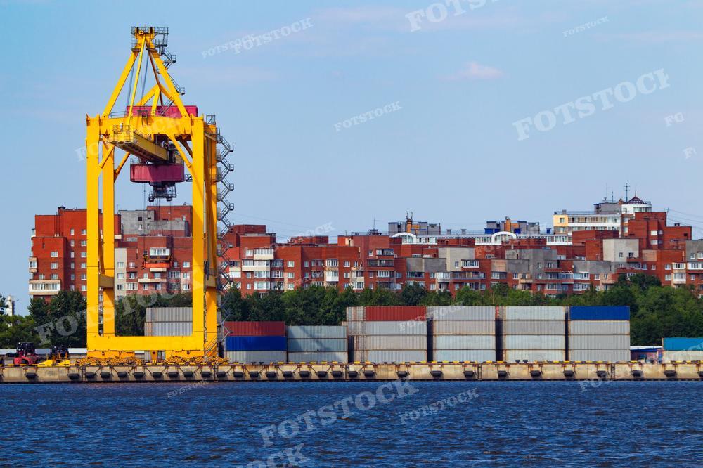 На фотографии изображен пустой морской грузовой порт, где отсутствуют суда. Порт расположен на фоне городских зданий. Видны причалы и краны, предназначенные для загрузки контейнеров на суда. 
Изображение может быть использовано для иллюстрации темы морских портов, логистики и международной торговли, а также для презентаций, статей или рекламных материалов, связанных с транспортной и логистической отраслями.